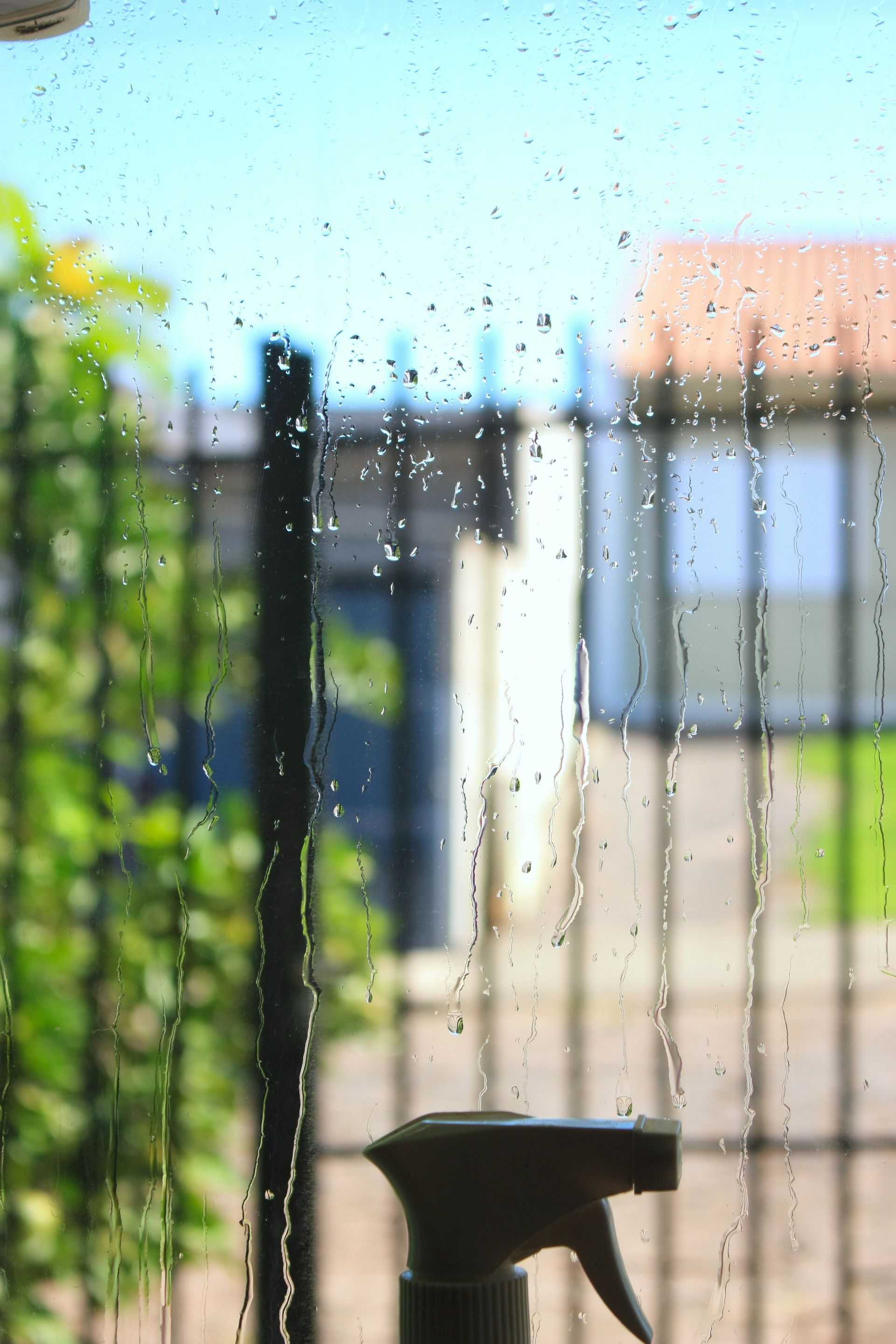 Raindrops streak down a window with spray bottle.